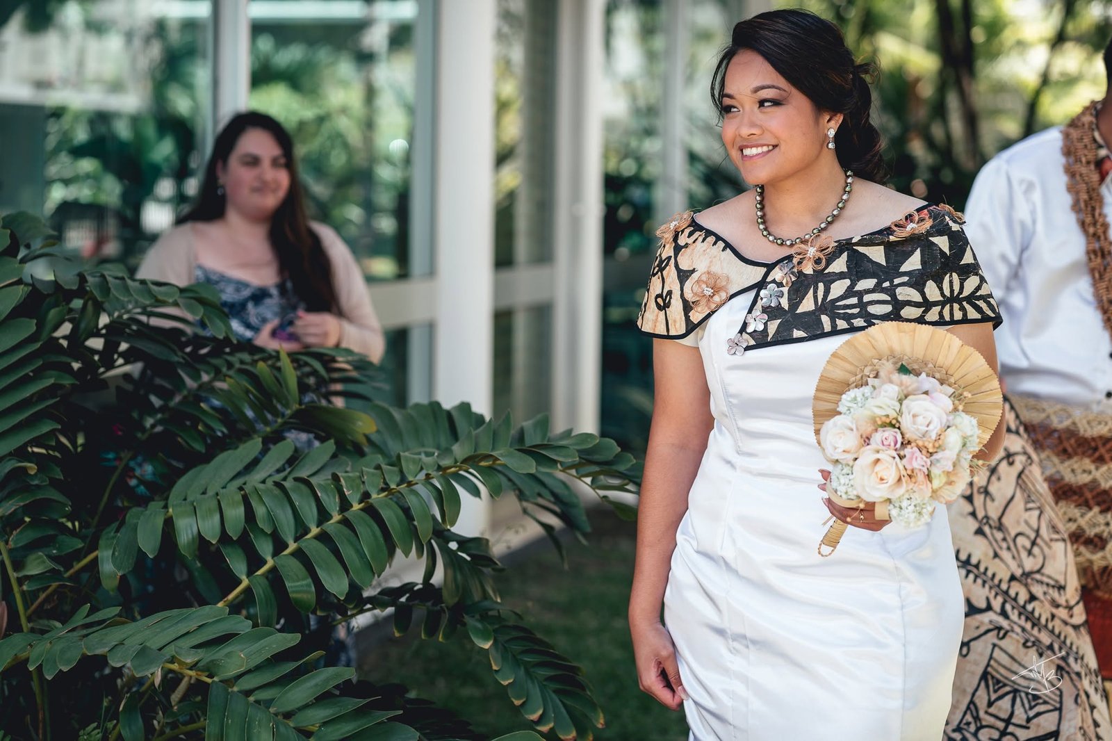 Entre les palmes, la mariée en tenue de mariage océanienne rejoint la cérémonie, bouquet en main — Timi M. Bourdet