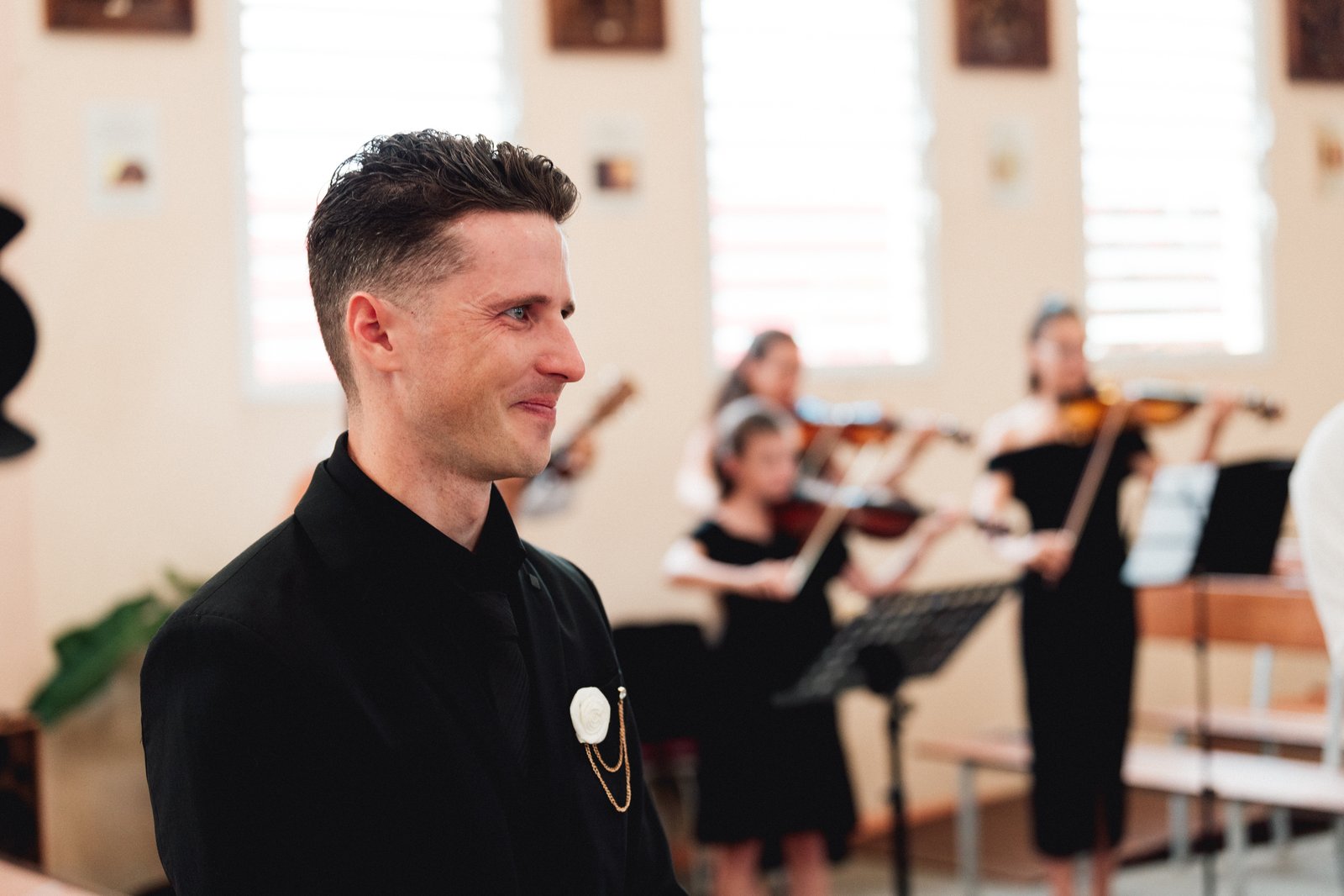 Le marié sourit, ému, pendant que les violonistes jouent dans l’église — Timi M. Bourdet
