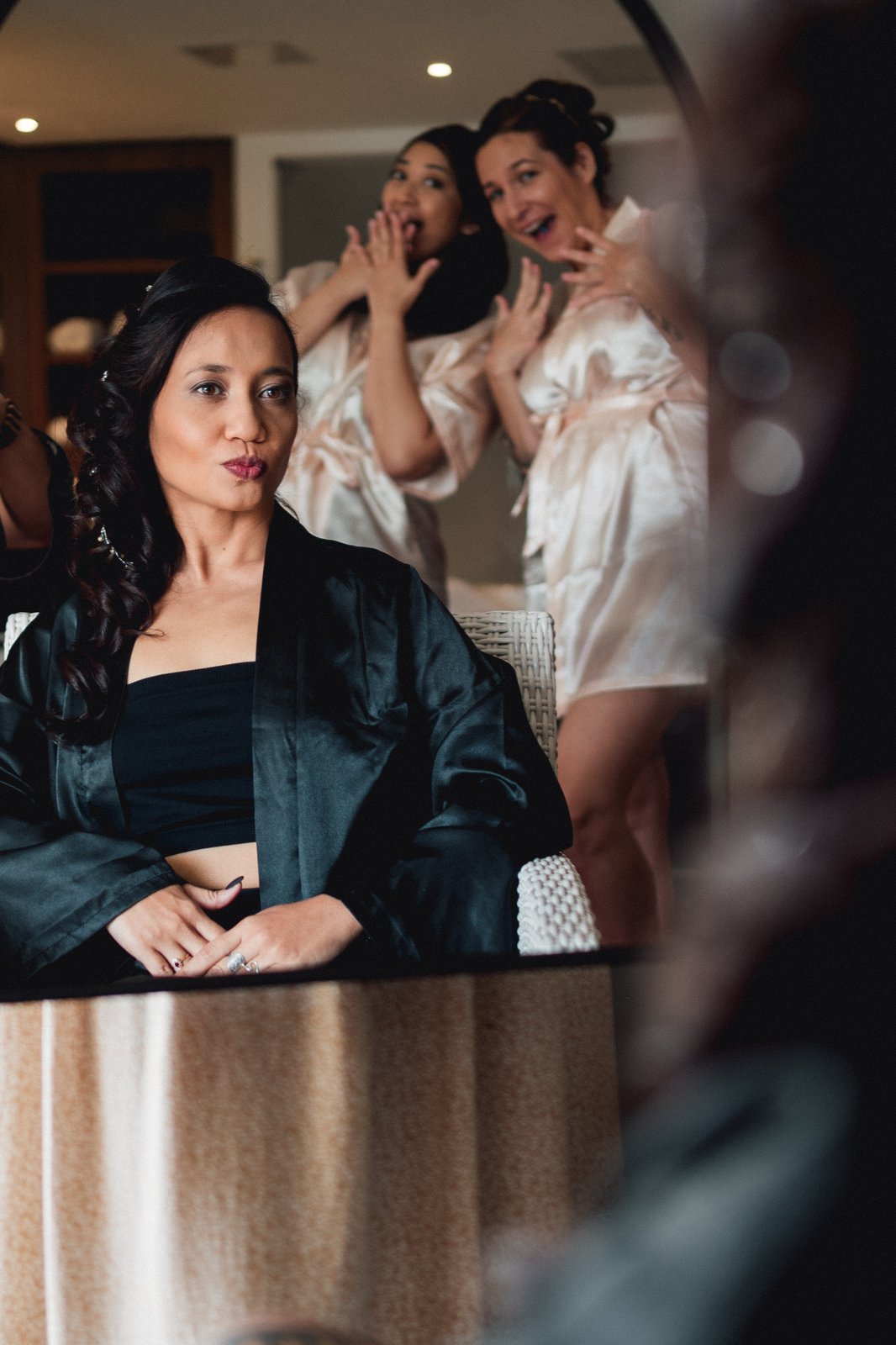 Dans le miroir, la mariée en kimono sombre garde son calme pendant que ses témoins s’amusent — Timi M. Bourdet