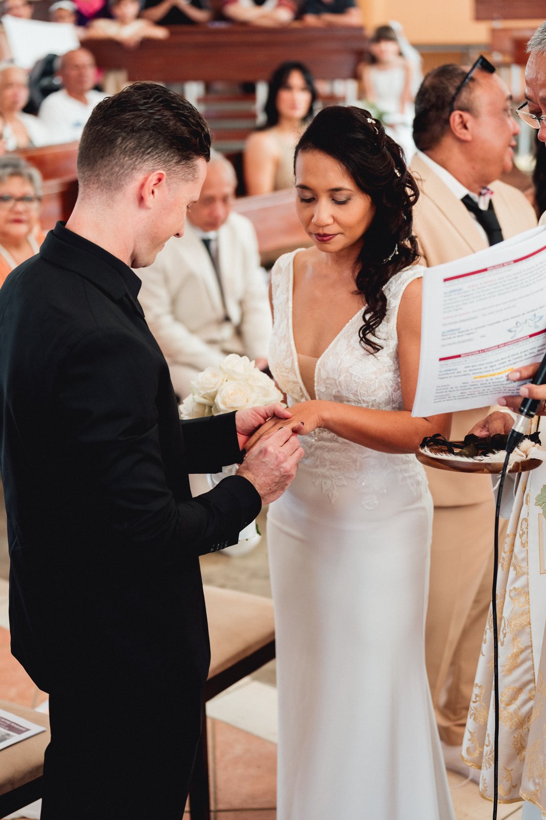 Échange des alliances devant le prêtre, la main de la mariée dans la lumière de l’église — Timi M. Bourdet