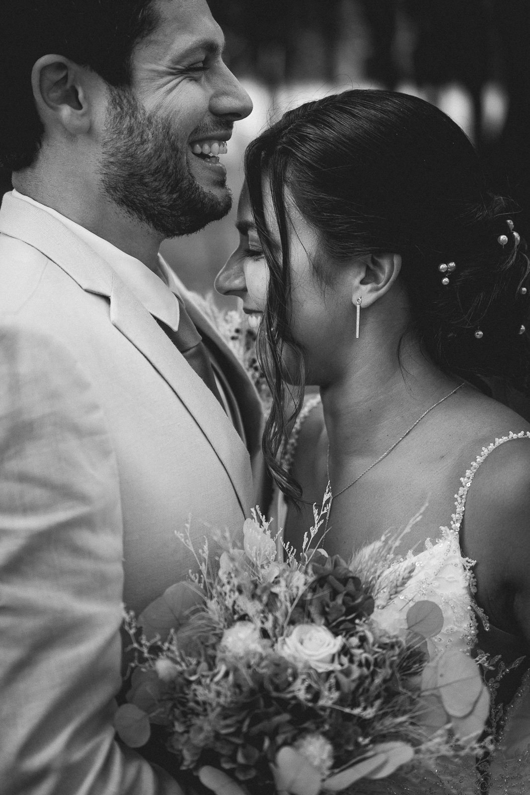 Front contre front, les mariés savourent un instant suspendu derrière le bouquet, en noir et blanc — Timi M. Bourdet