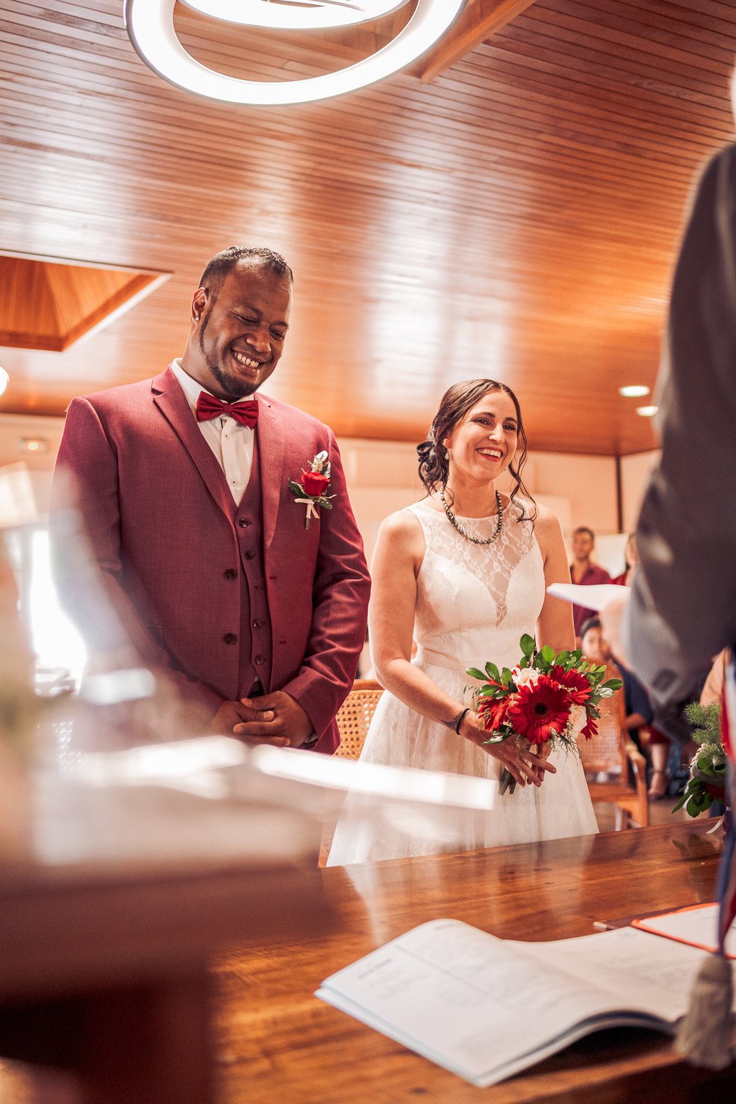 Les mariés souriants devant l’officiant, sous le plafond de bois de la mairie — Timi M. Bourdet