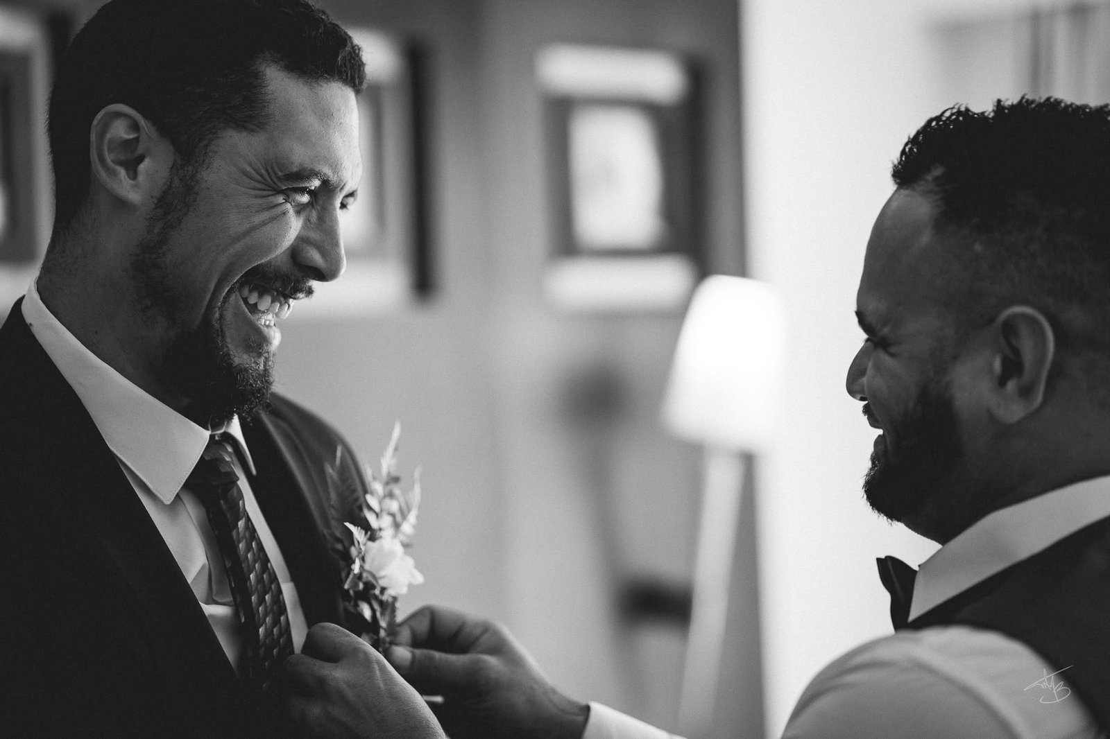 Éclat de rire pendant qu’un ami épingle la boutonnière du marié, préparatifs en noir et blanc — Timi M. Bourdet