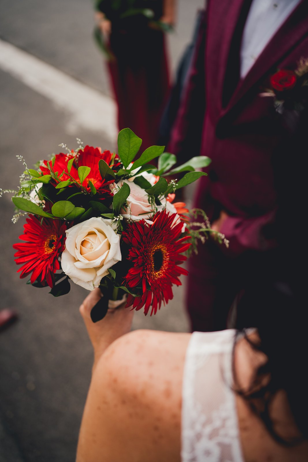 Le bouquet de gerberas rouges et de roses crème de la mariée, costume bordeaux en arrière-plan — Timi M. Bourdet