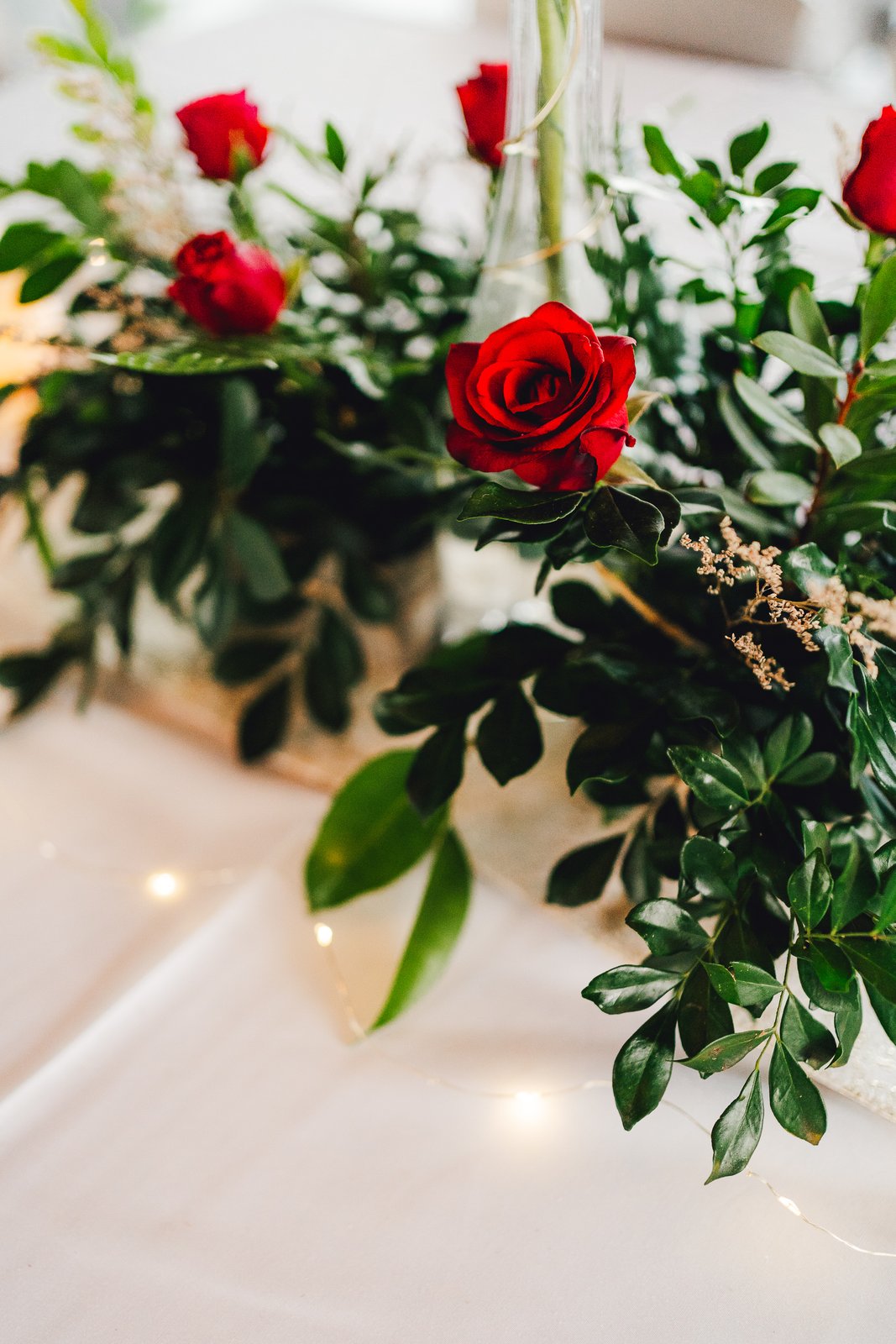Centre de table aux roses rouges, feuillages et guirlande lumineuse — Timi M. Bourdet