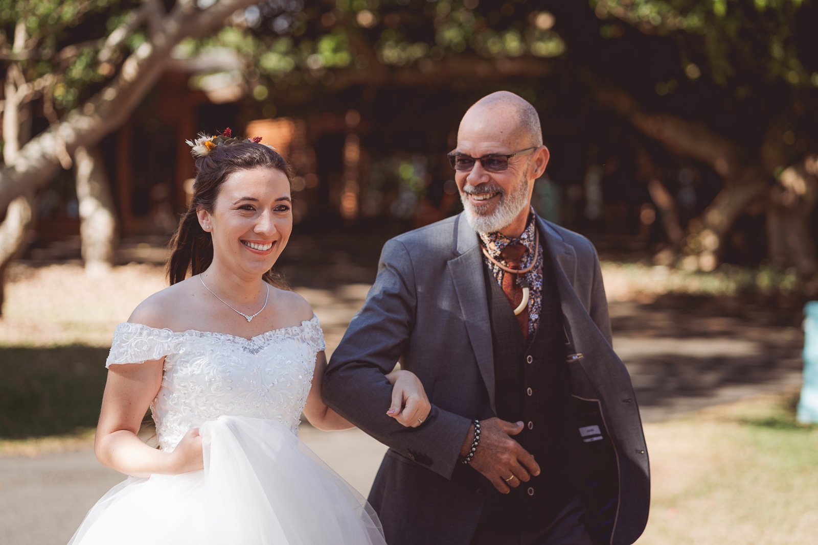 La mariée rayonnante au bras de son père, en chemin vers la cérémonie — Timi M. Bourdet